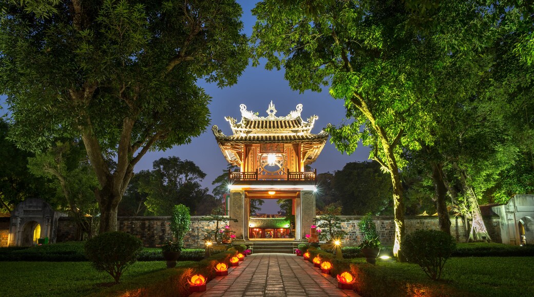 Une porte chinoise traditionnelle, dotée d’une architecture richement décorée, entourée d’une végétation luxuriante et illuminée par des lanternes.