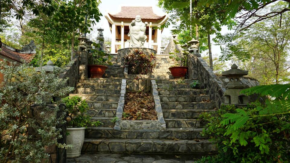 A stone staircase leading to a pagoda with a traditional roof, surrounded by lush greenery.