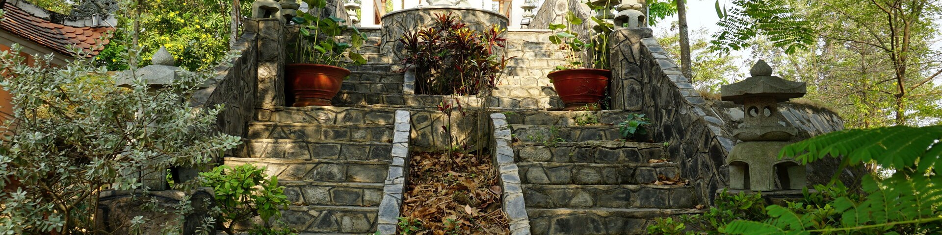 Una escalera de piedra conduce a una pagoda con techo tradicional, rodeada de abundante vegetación.