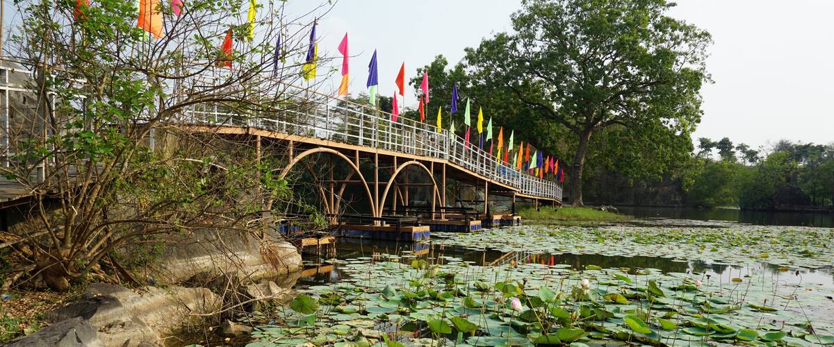 A bridge with colorful flags, a pond with lily pads, and trees in the background.