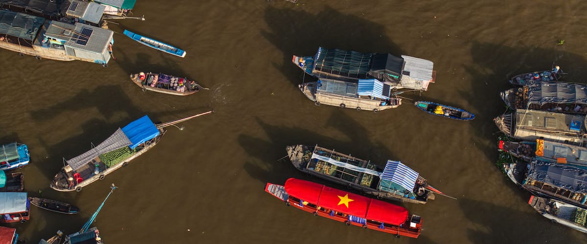 An aerial view of a river with numerous boats docked along the banks, some with canopies and others with open sides.