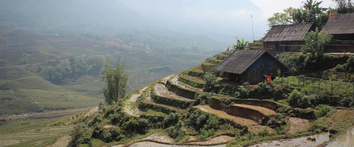Terraced rice fields, a wooden house, and mountains in the background.