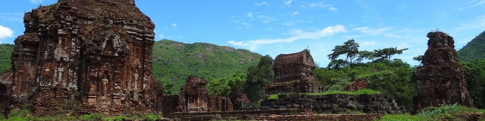 Ancient stone ruins with multiple structures, surrounded by lush greenery and hills.