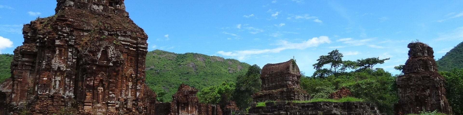 Ruínas de pedra antigas com várias estruturas, rodeadas por vegetação exuberante e colinas.