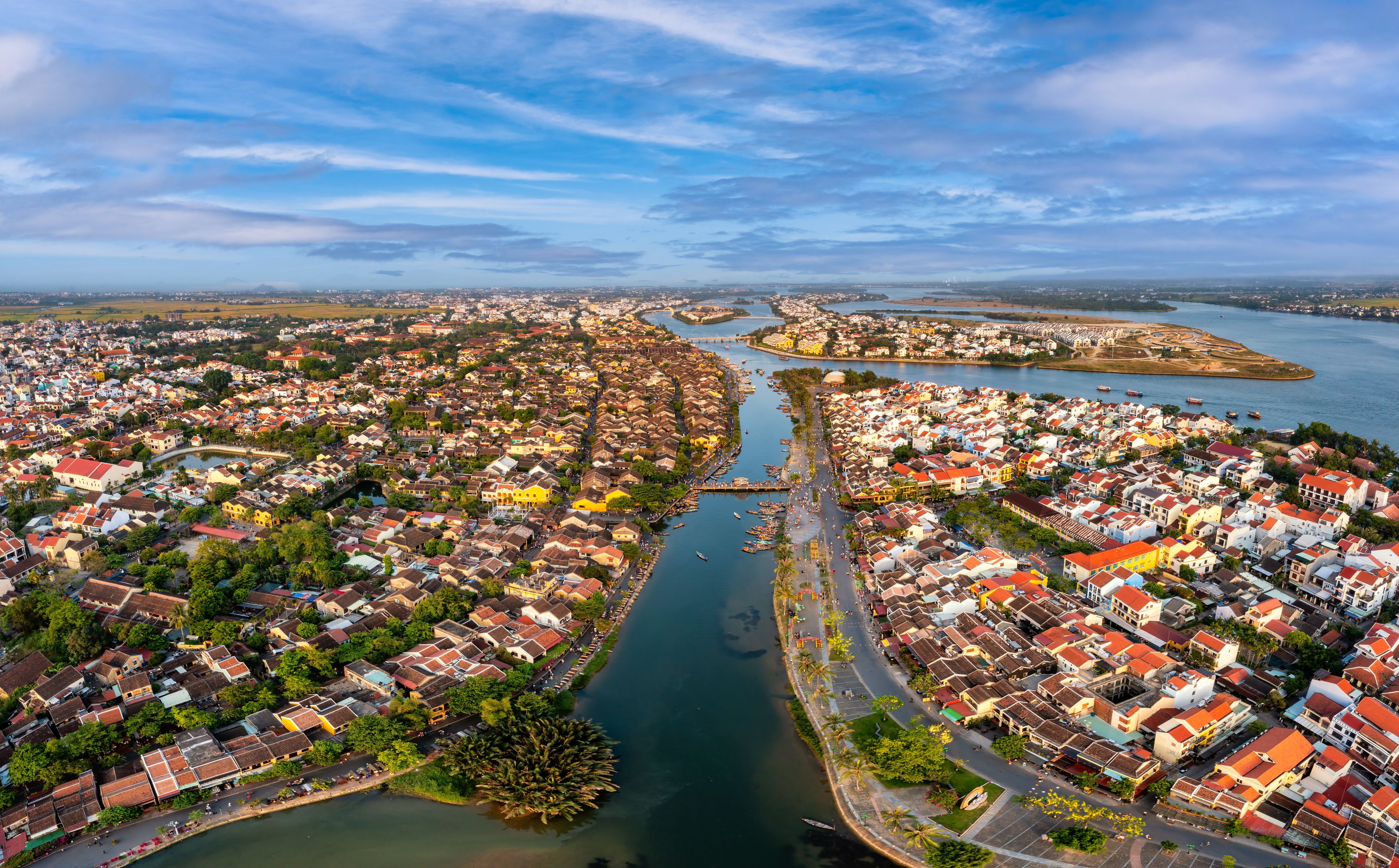 An aerial view of a coastal city with dense housing, a river, and a distant island.