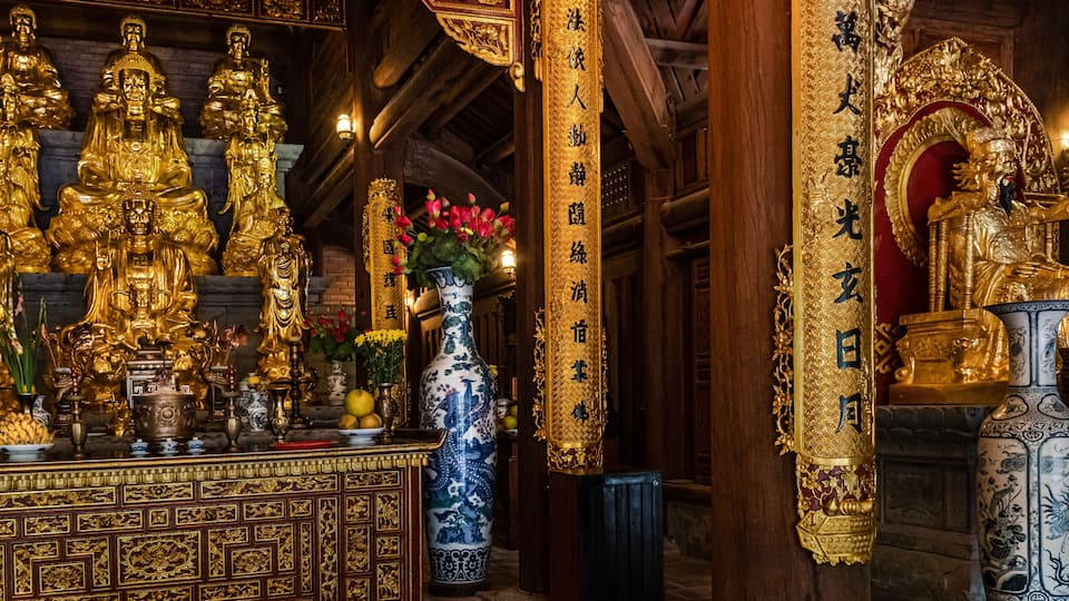 Interior de un templo con estatuas doradas, un jarrón grande y decoraciones ornamentales.
