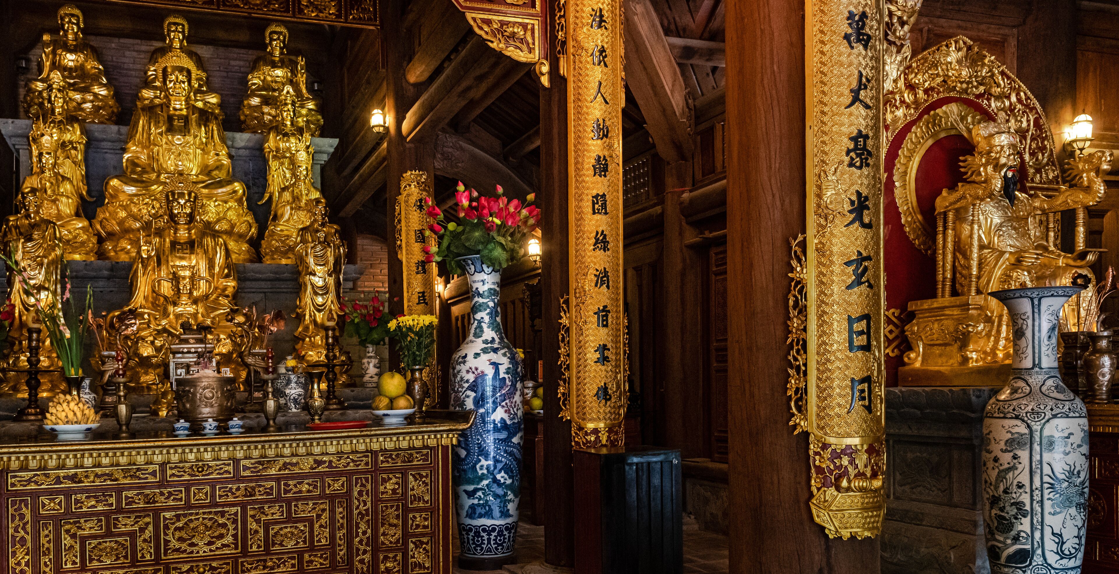 A temple interior with golden statues, a large vase, and ornate decorations.