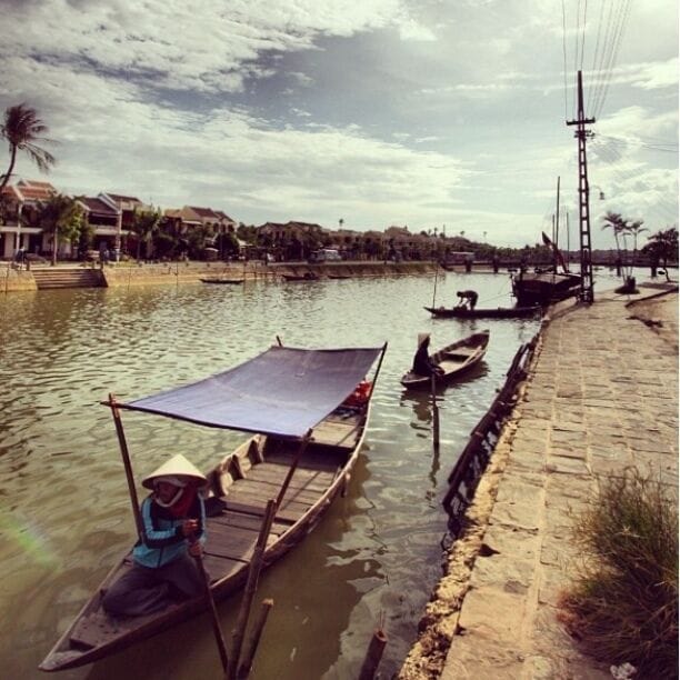 A river with boats, a person in a boat, and a bridge in the background.