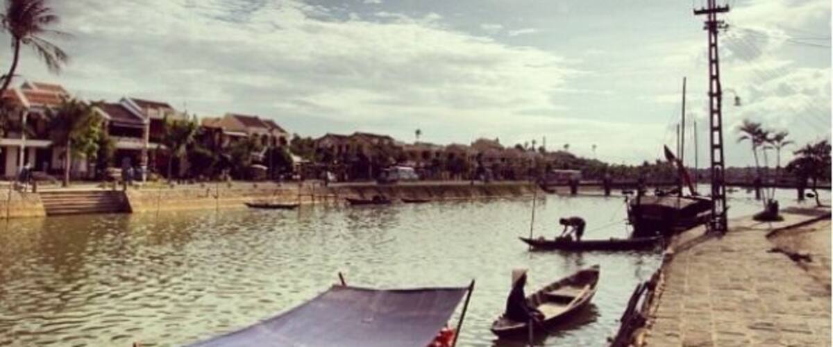 A river with boats, a person in a boat, and a bridge in the background.