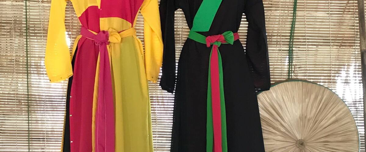 Two mannequins dressed in colorful dresses with long sleeves and belts, against a bamboo backdrop.