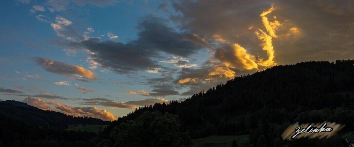 A sunset over a forested hill with clouds illuminated by the sun.