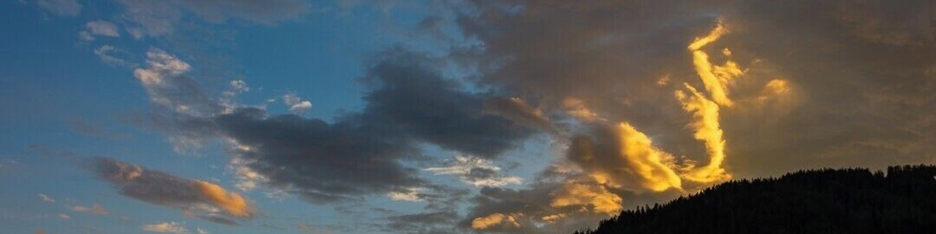 A sunset over a forested hill with clouds illuminated by the sun.