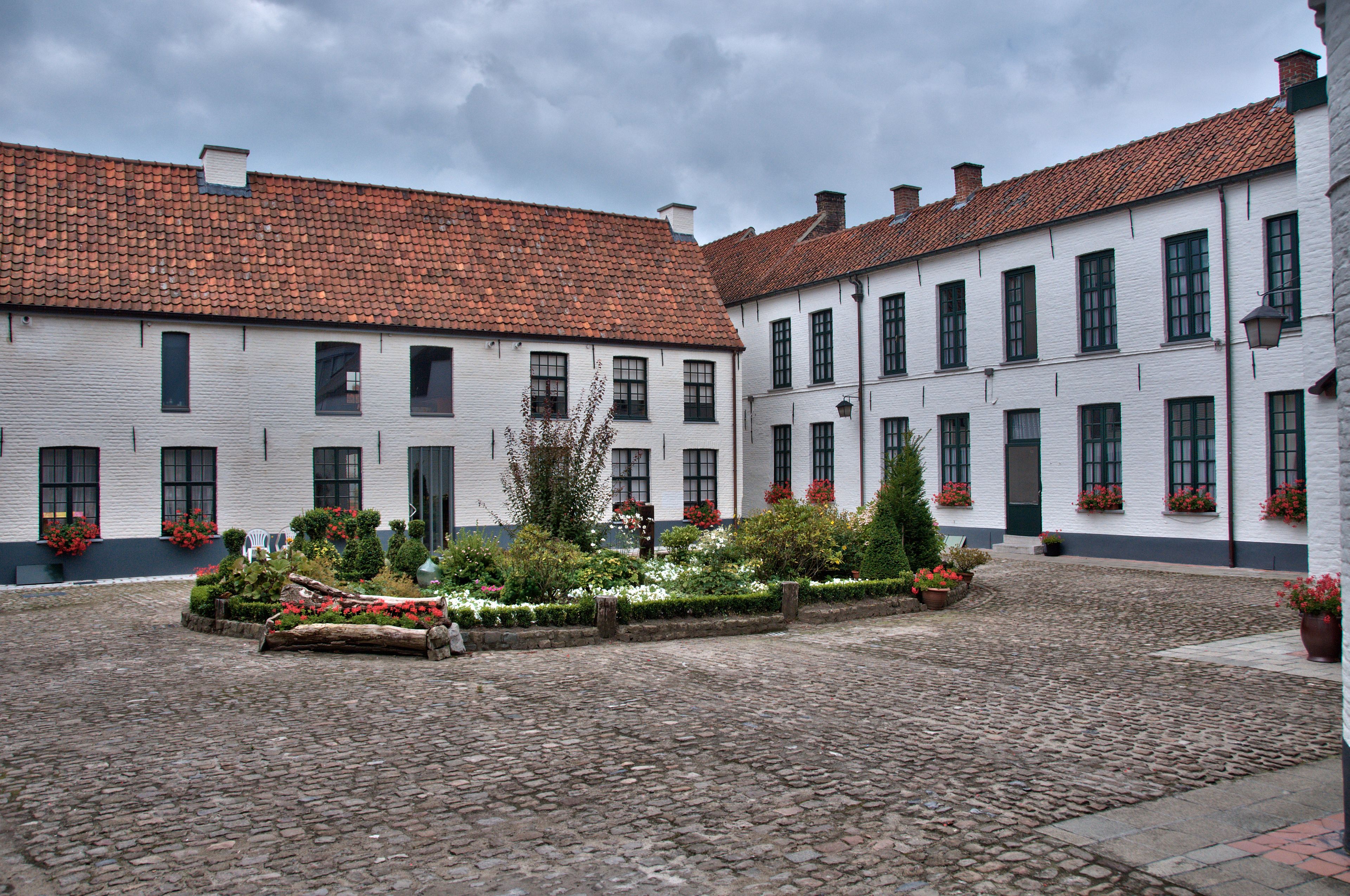 Um pátio com pavimento de pedra, edifícios brancos com telhados de terracota e floreiras nas janelas.