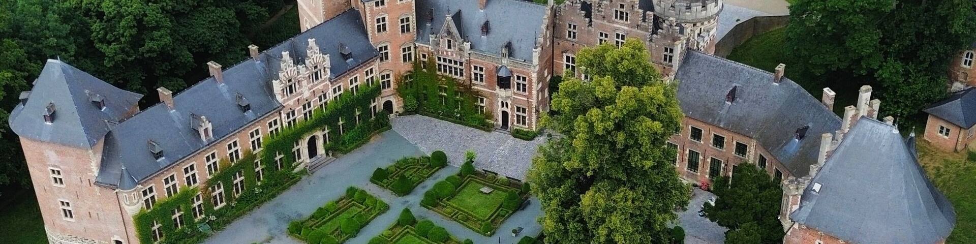 An aerial view of a large, historic castle with a formal garden, surrounded by lush green fields and trees.