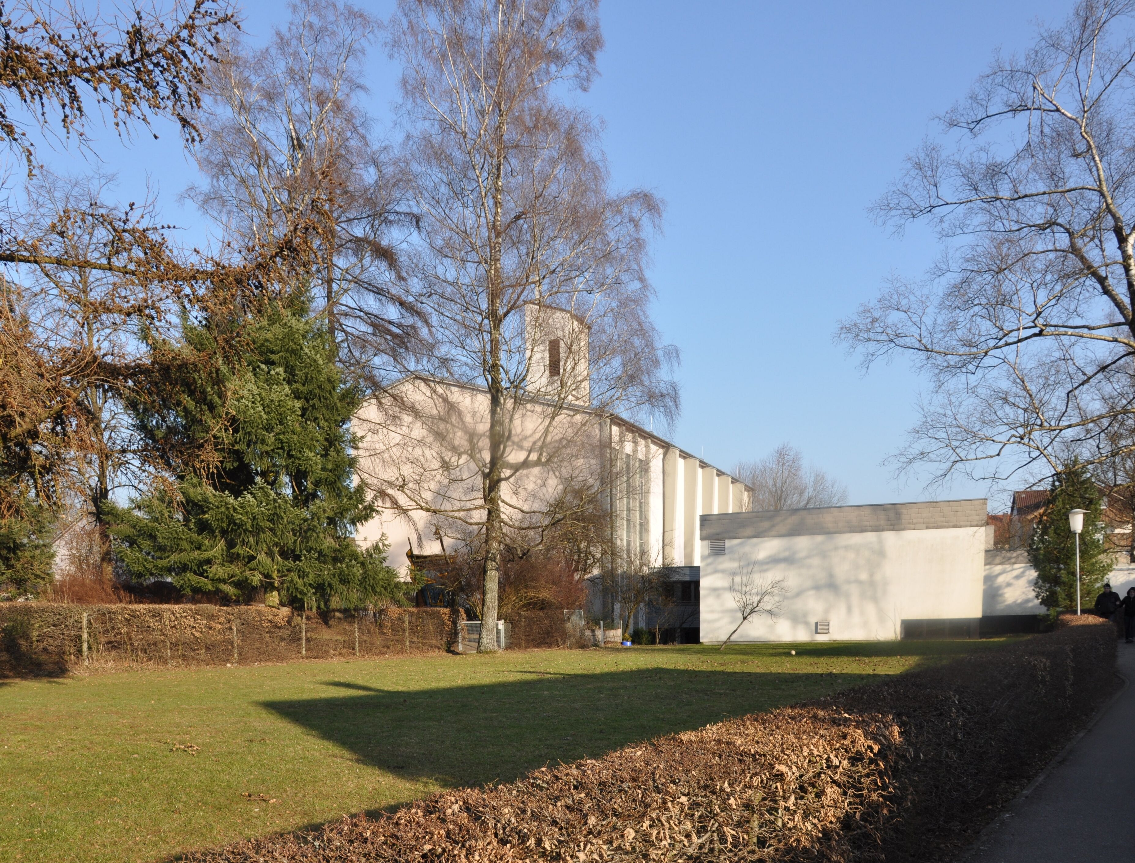 A building with a white facade and a chimney, surrounded by trees and a grassy area.