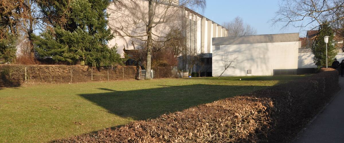 A building with a white facade and a chimney, surrounded by trees and a grassy area.