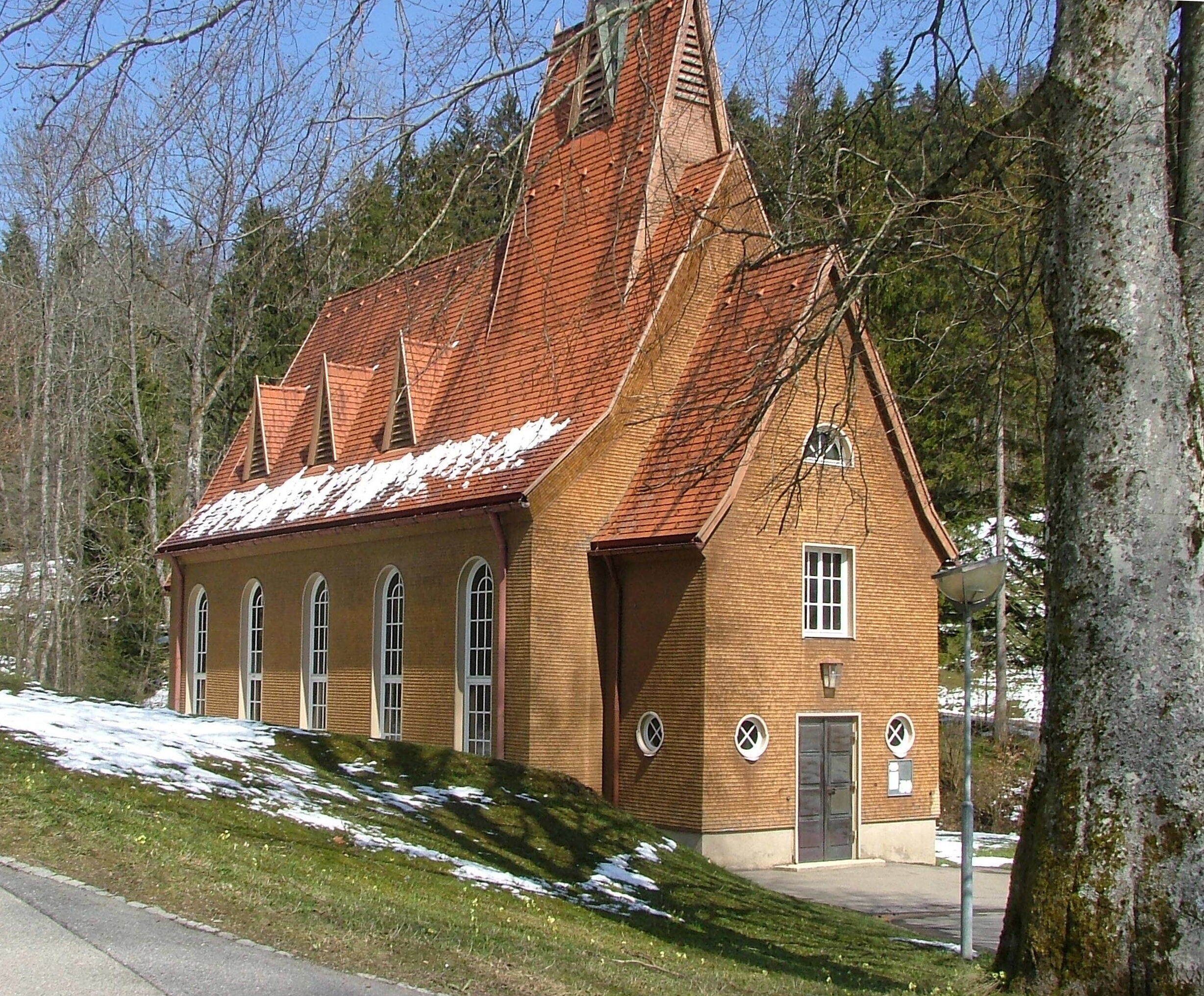 A brick building with a steeply pitched roof, arched windows, and a door with a cross symbol.