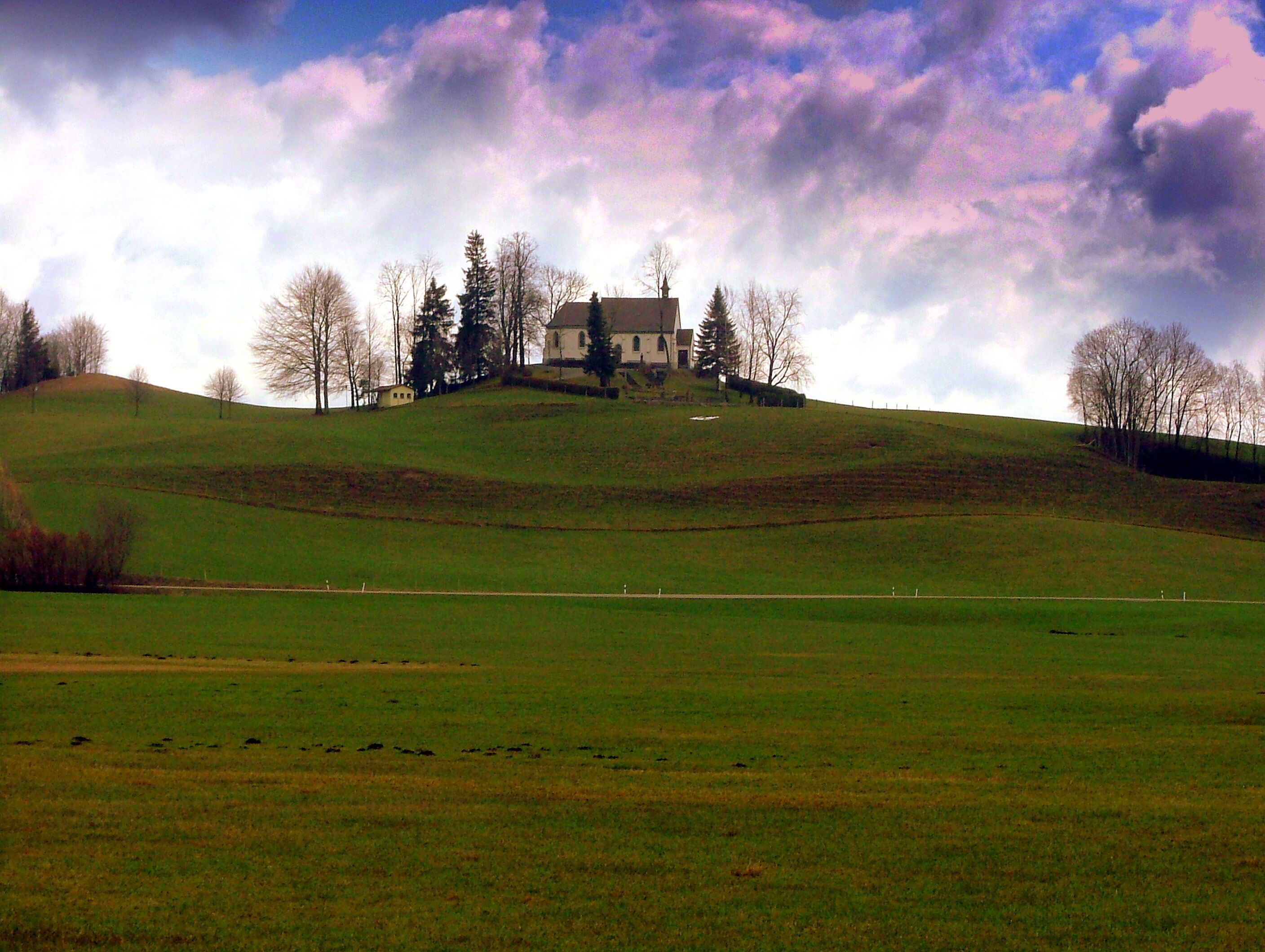 A large house on a hill with a green field in the foreground.