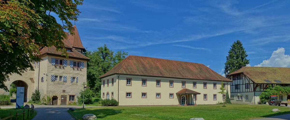 A historic building with a steep roof and a large arched entrance, surrounded by a well-maintained lawn and a paved pathway.