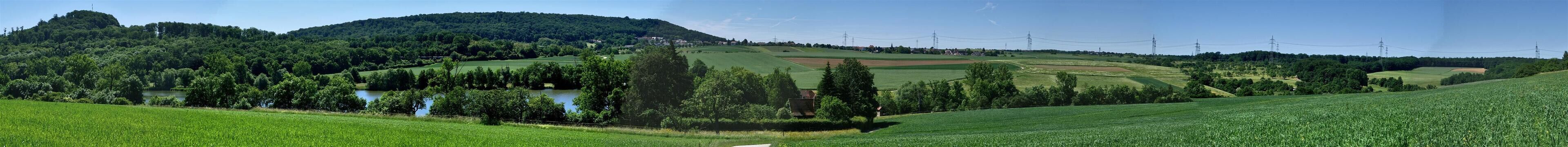 A lush green landscape with rolling hills, a river, and distant power lines.