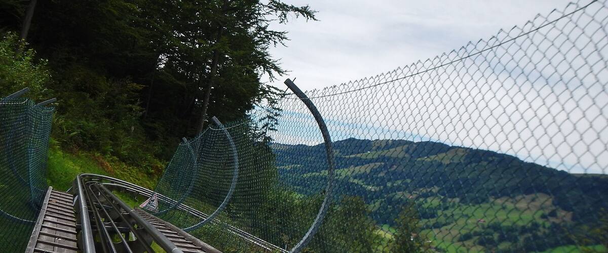 A railway track with a chain-link fence and a mountainous landscape in the background.