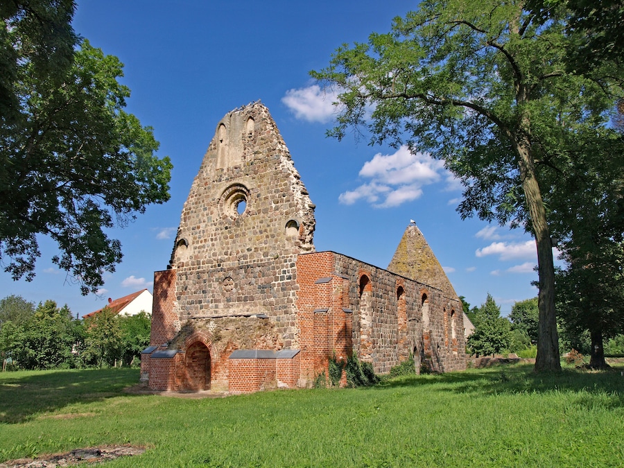 An ancient stone church with a tall bell tower and a smaller spire, surrounded by lush green grass and trees.