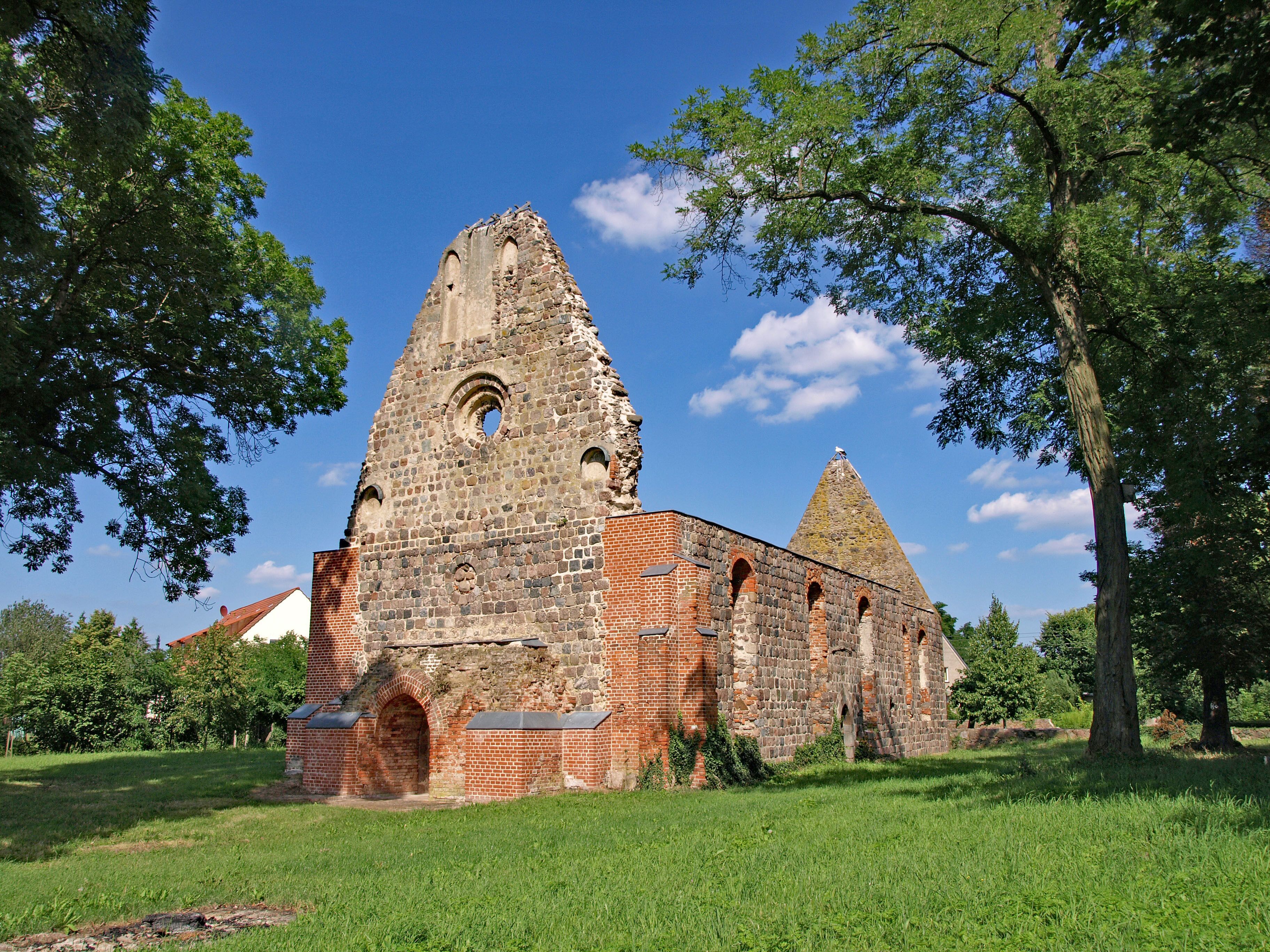 An ancient stone church with a tall bell tower and a smaller spire, surrounded by lush green grass and trees.