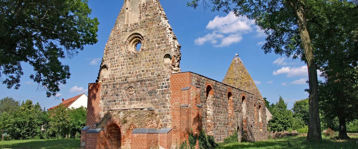 An ancient stone church with a tall bell tower and a smaller spire, surrounded by lush green grass and trees.
