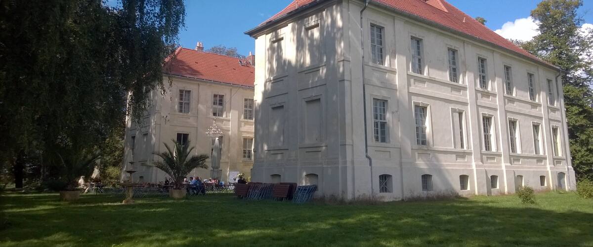 A large, historic building with a red roof and multiple windows, surrounded by a well-maintained lawn and trees.