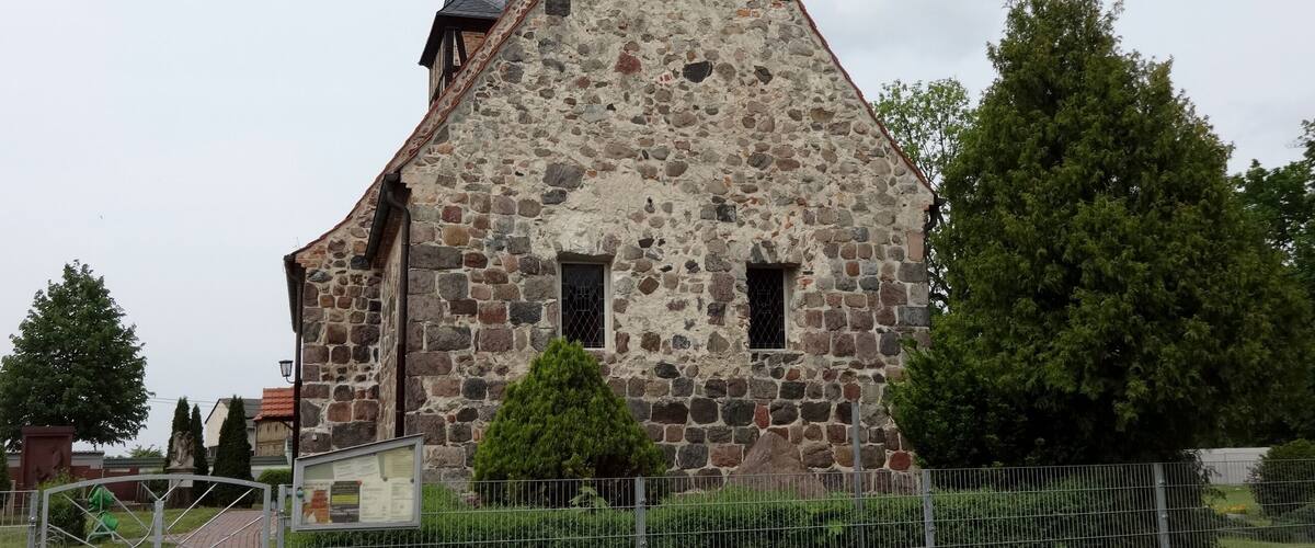 A stone church with a pointed roof and a weather vane.