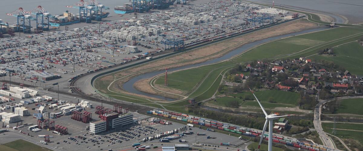 An industrial port with shipping containers, cranes, and a wind turbine.