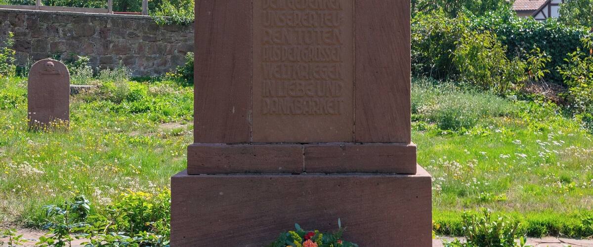 A statue of a soldier on a pedestal with a plaque, surrounded by flowers.