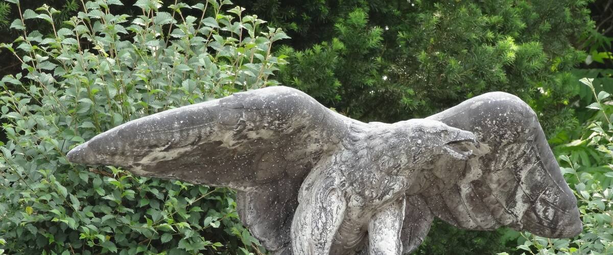 A stone eagle statue on a rock with green foliage in the background.