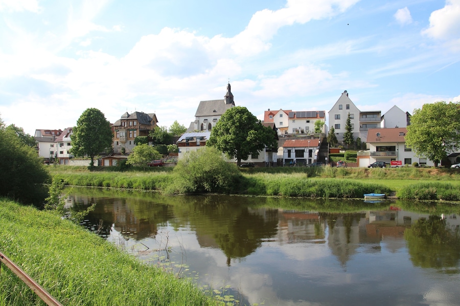Un río tranquilo con un bote pequeño, rodeado de exuberante vegetación y edificios tradicionales europeos.