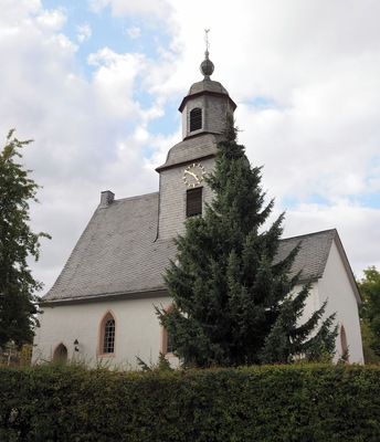 Una iglesia con una torre del reloj y un árbol grande en primer plano.