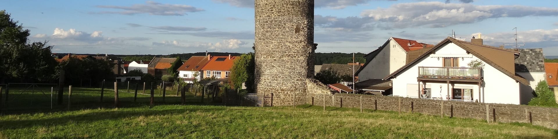 A stone tower with a conical roof, surrounded by a grassy field and residential buildings.