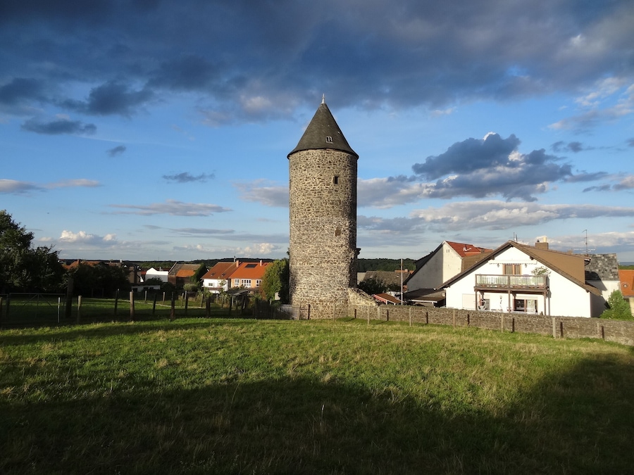 A stone tower with a conical roof, surrounded by a grassy field and residential buildings.