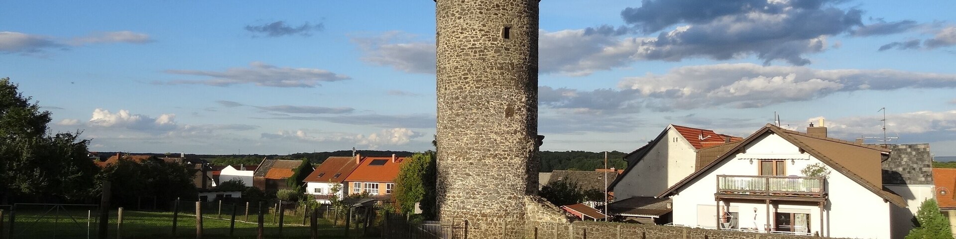 Una torre de piedra con techo cónico, rodeada por un campo cubierto de hierba y edificios residenciales.