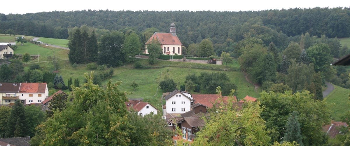 A church surrounded by lush greenery and houses on a hillside.