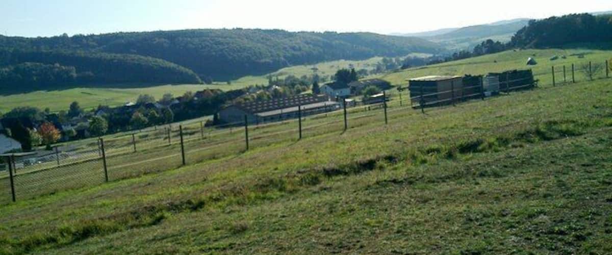 A rural landscape with rolling hills, a fenced area, and a building in the distance.