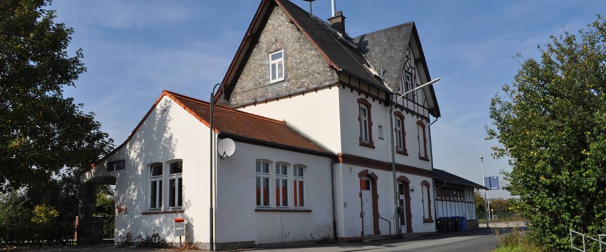 A traditional white building with a steeply pitched roof and a chimney, located beside a road with a clear sky.