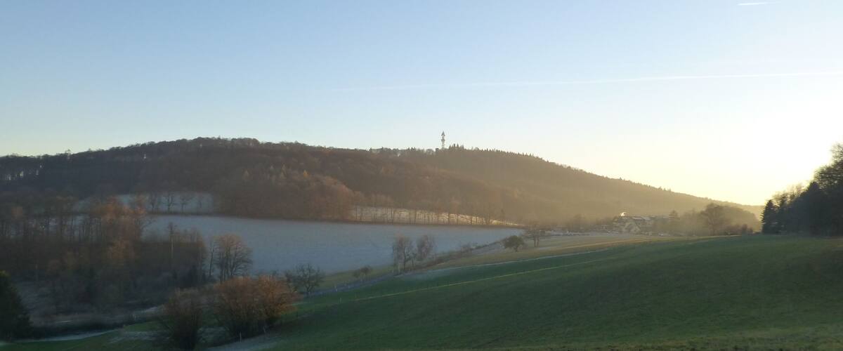 A serene landscape with a lake, a hill with trees, and a clear sky.