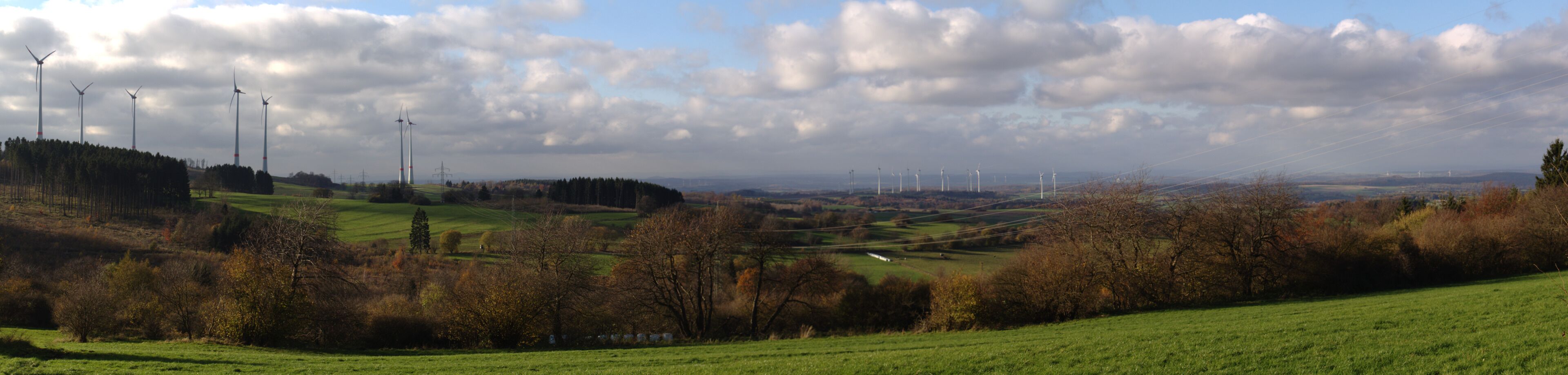 A landscape with wind turbines, rolling hills, and a cloudy sky.