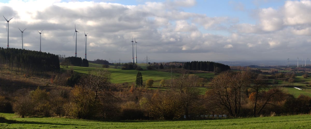 A landscape with wind turbines, rolling hills, and a cloudy sky.