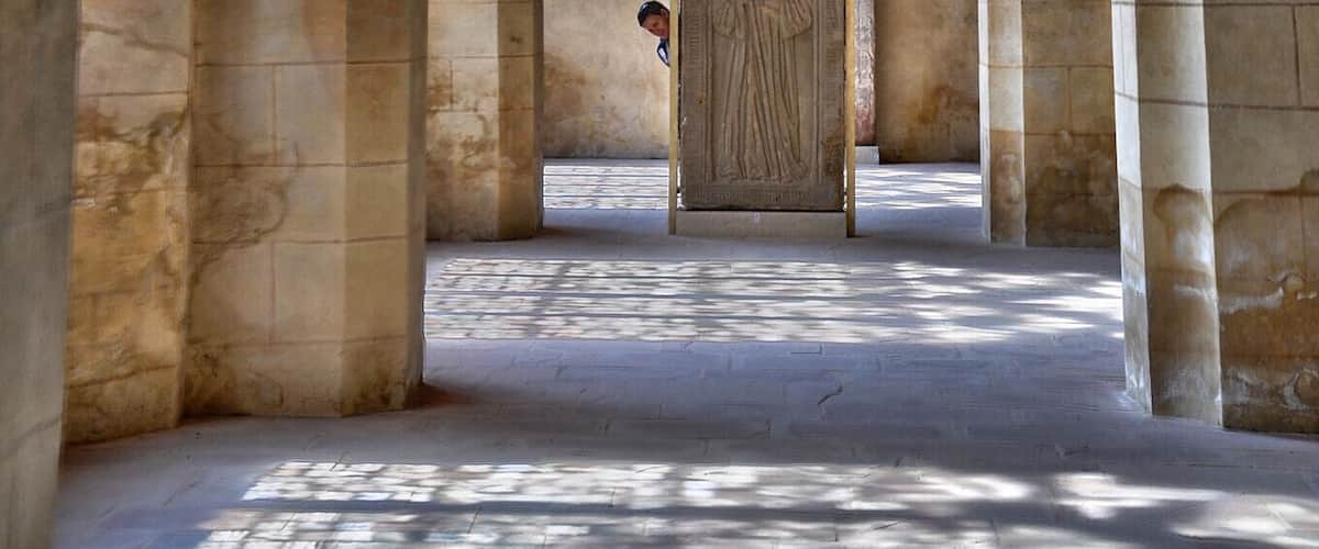 An arched corridor with stone columns and a wooden door at the end.