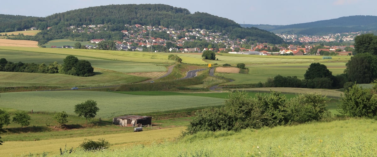 A rural landscape with rolling hills, a winding road, and a small village in the distance.