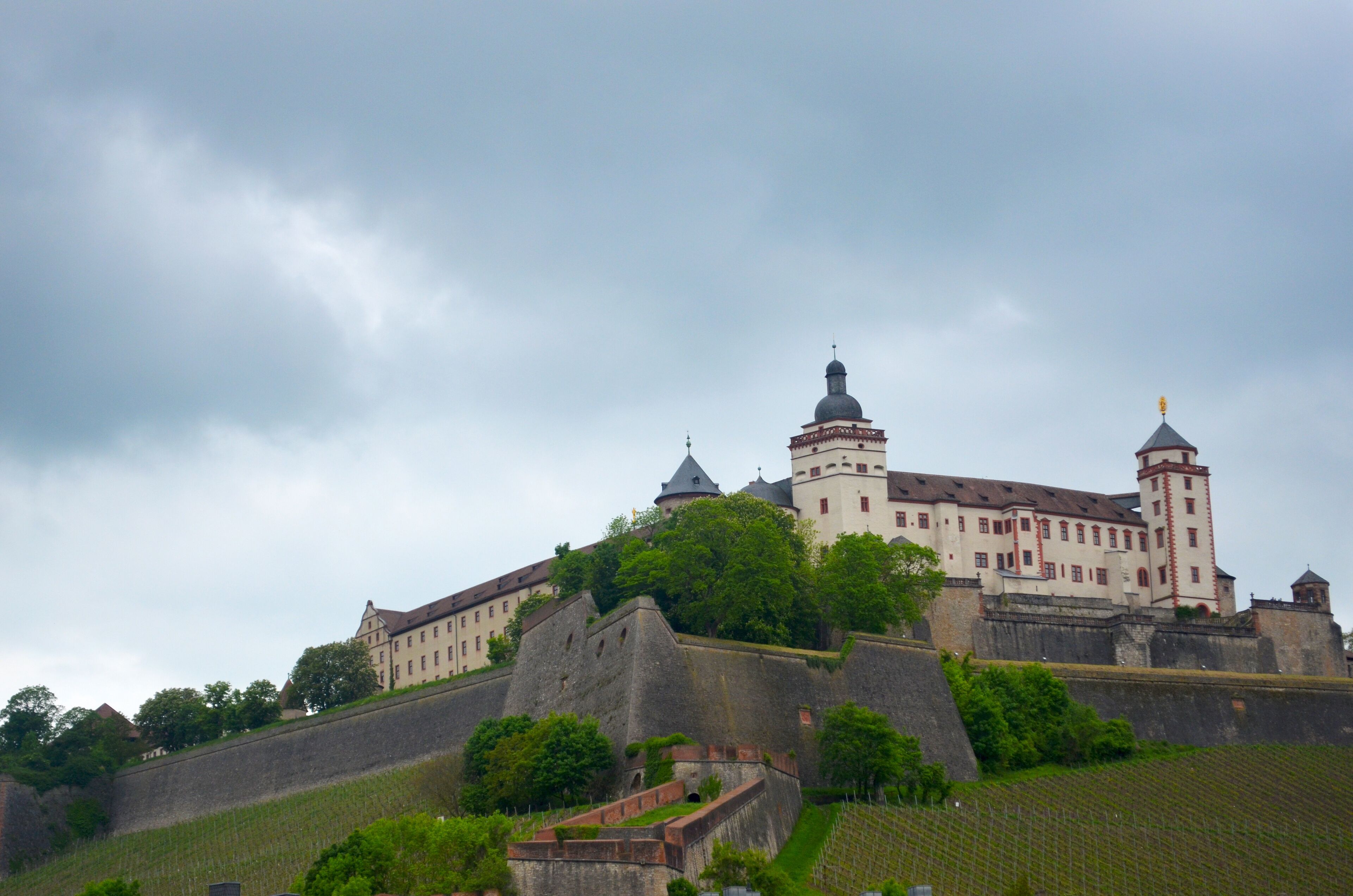 A historic castle with multiple towers and a fortified wall, surrounded by lush greenery.