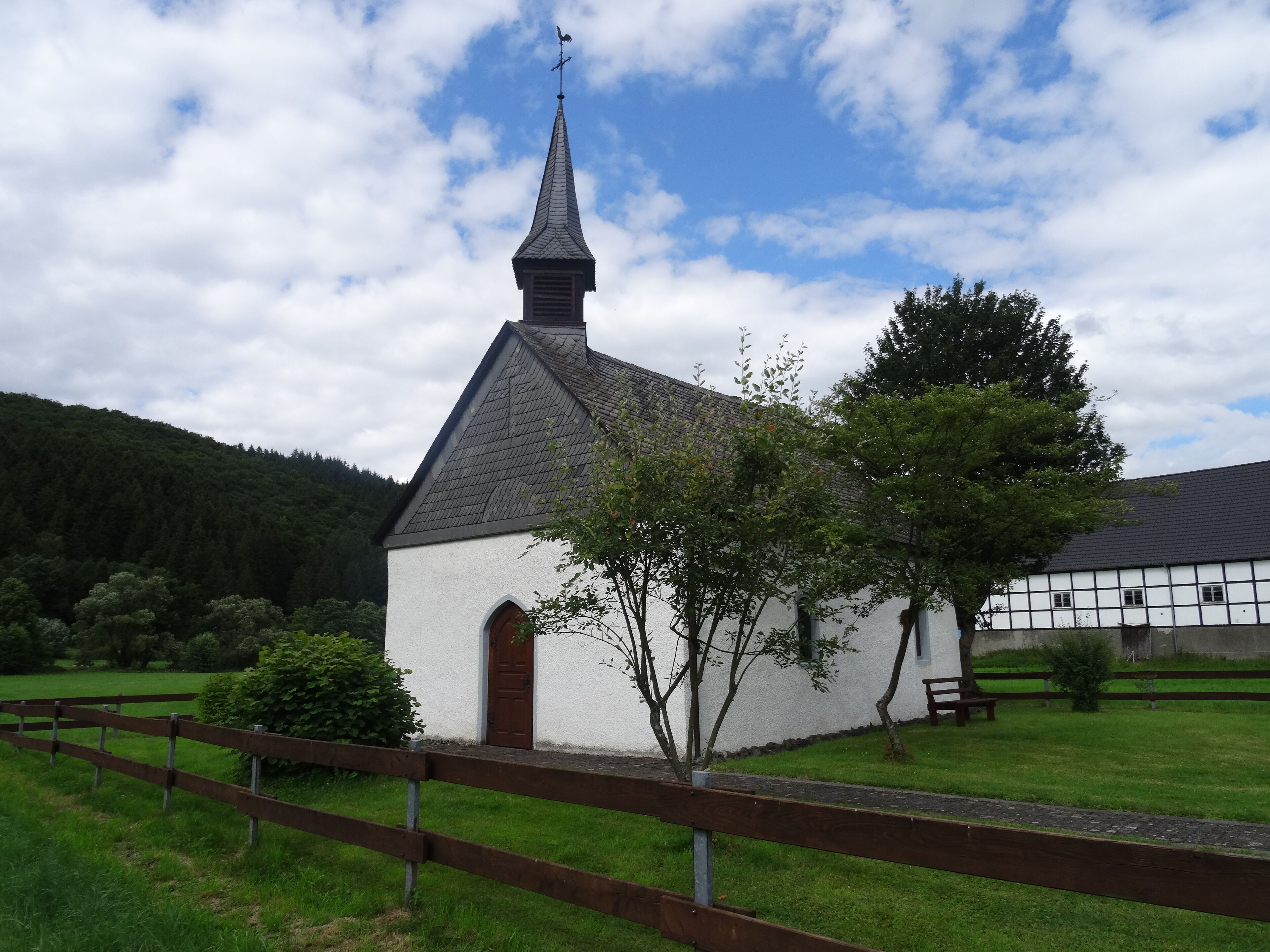 A white church with a pointed steeple and a weather vane, surrounded by green grass and trees.