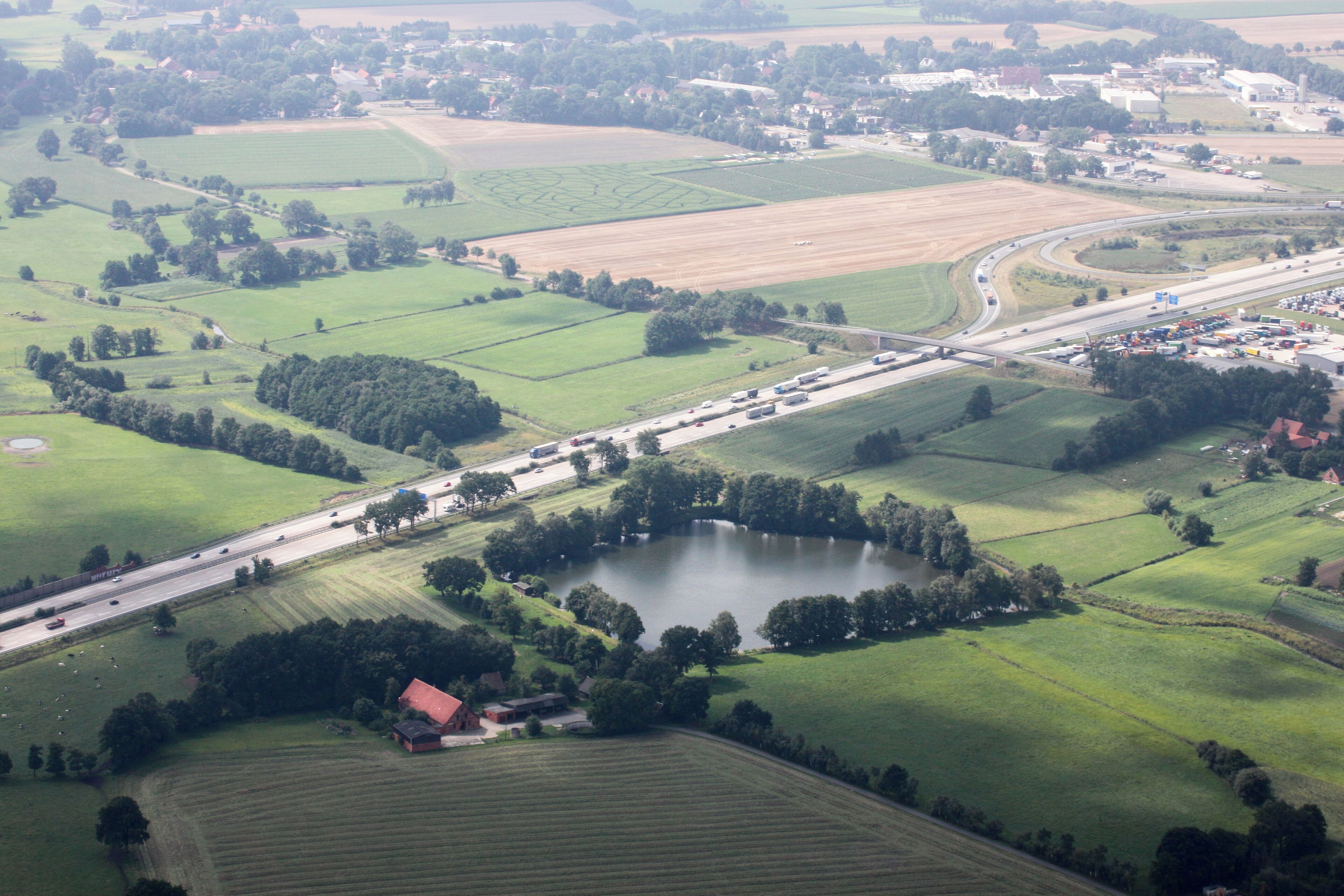 An aerial view of a rural landscape with fields, a lake, and a highway.