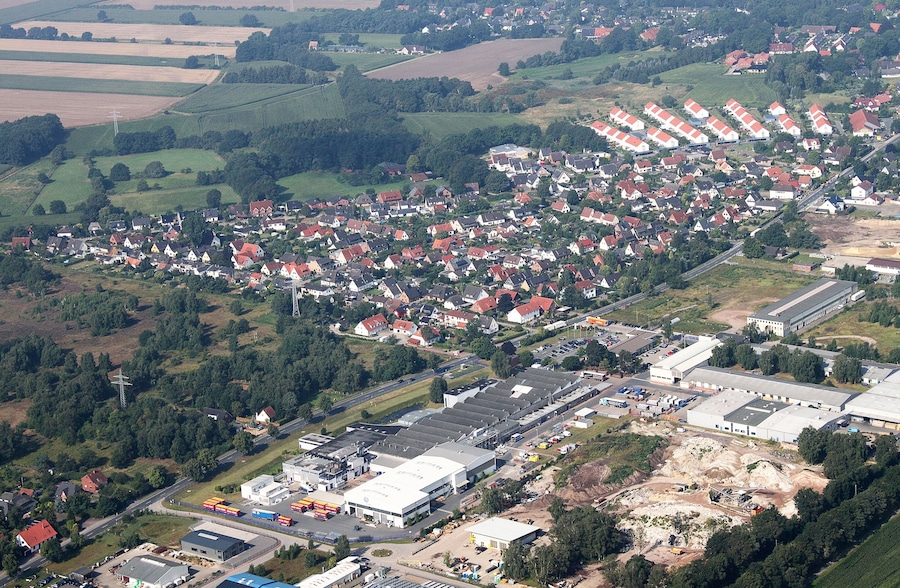 An aerial view of a residential area with houses, a large industrial complex, and surrounding fields.